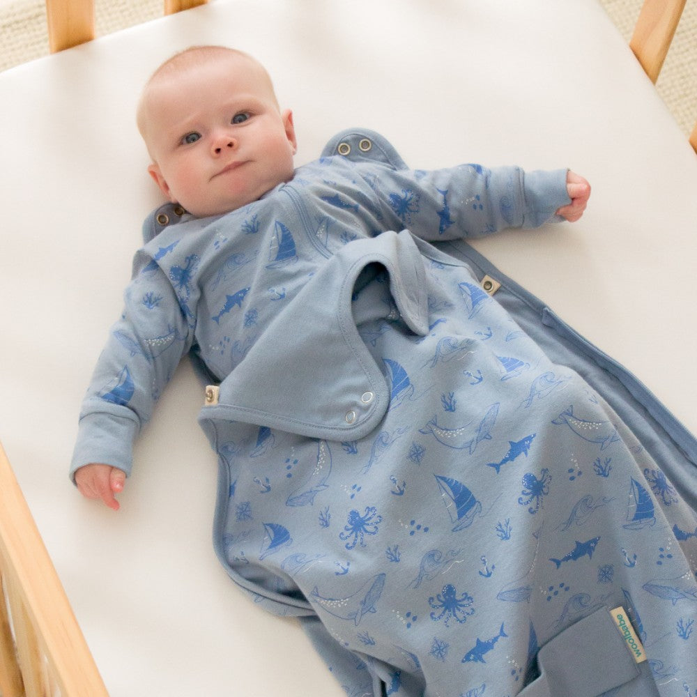 Baby lying on a white surface wearing a blue onesie with sea creature patterns.