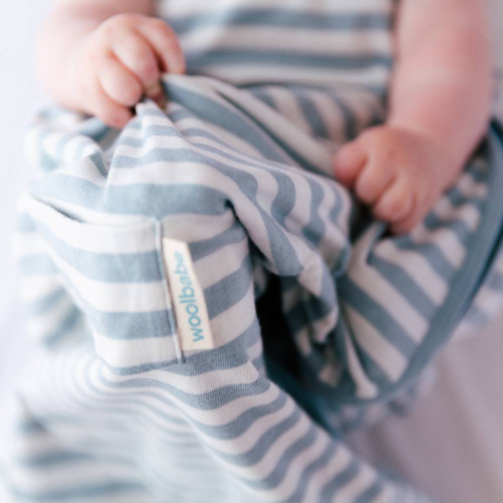Baby holding a blue and white striped blanket with 'woolbabe' label.