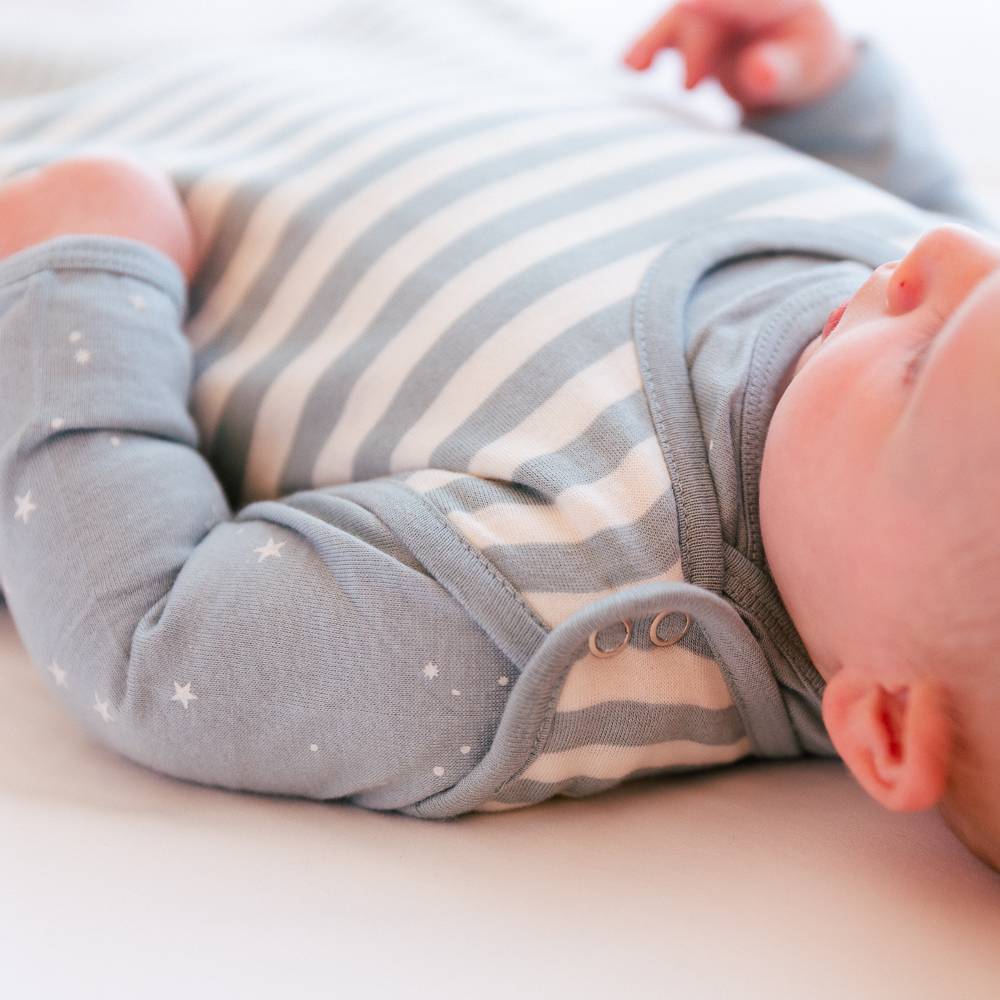 Baby wearing a gray and white striped woolbabe lying on a light surface