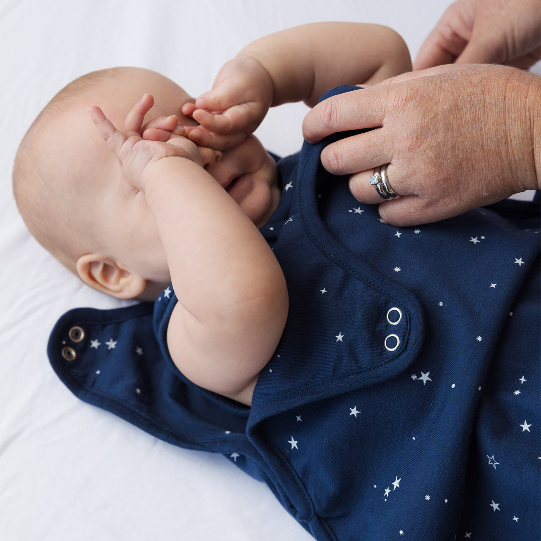 Baby wearing a navy blue baby sleeping bag with star patterns, held by an adult hand.