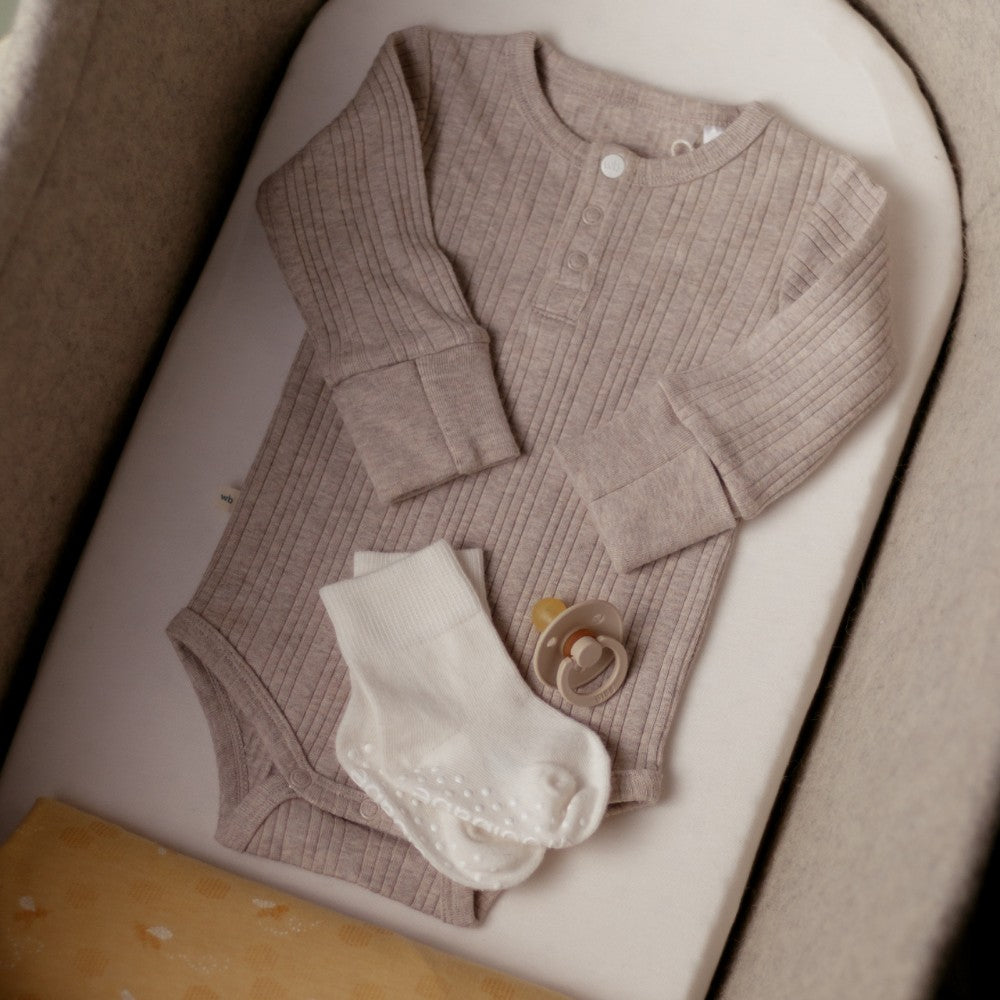 Baby outfit with brown ribbed woolbabe bodysuit and white baby socks and pacifier gift pack on a white surface.