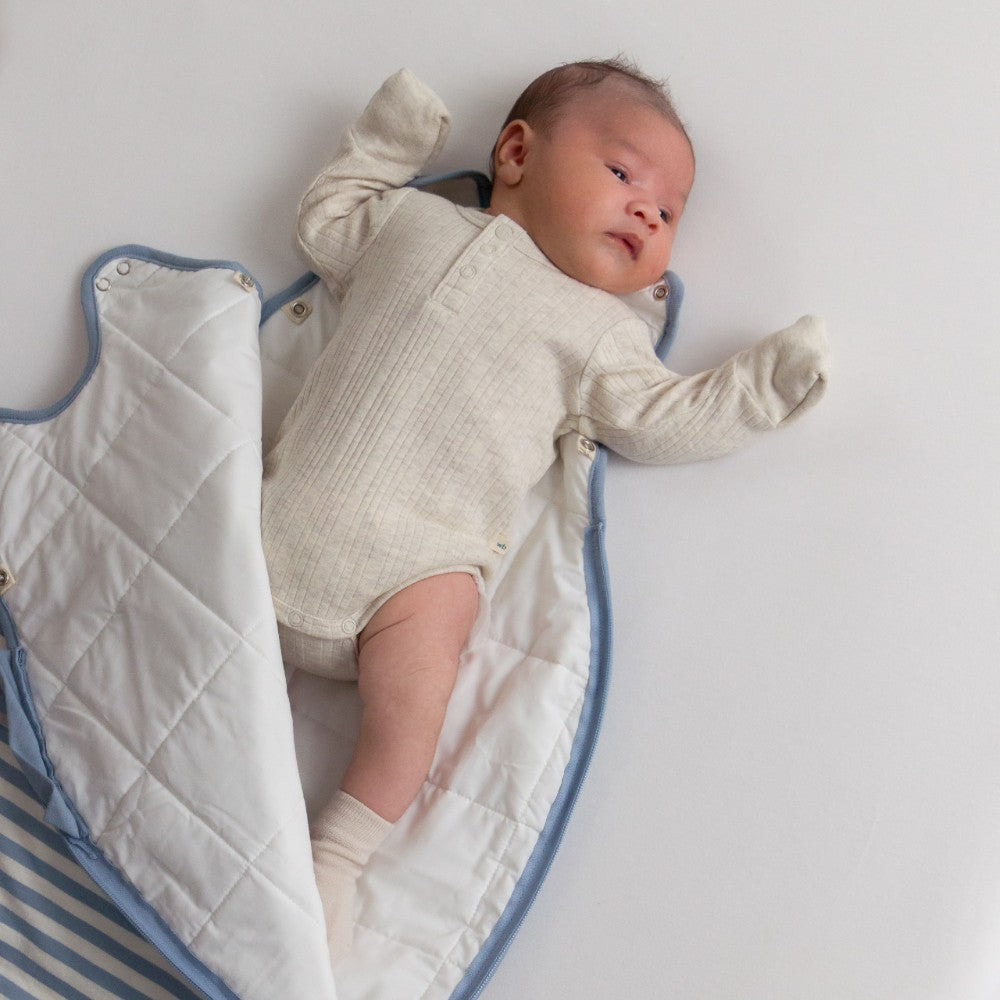Baby lying on a woolbabe sleeping bag wearing a oat colour rib merino bodysuit 