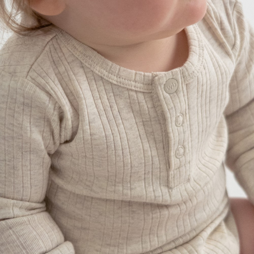 Close-up of a child wearing a beige ribbed long-sleeve shirt.