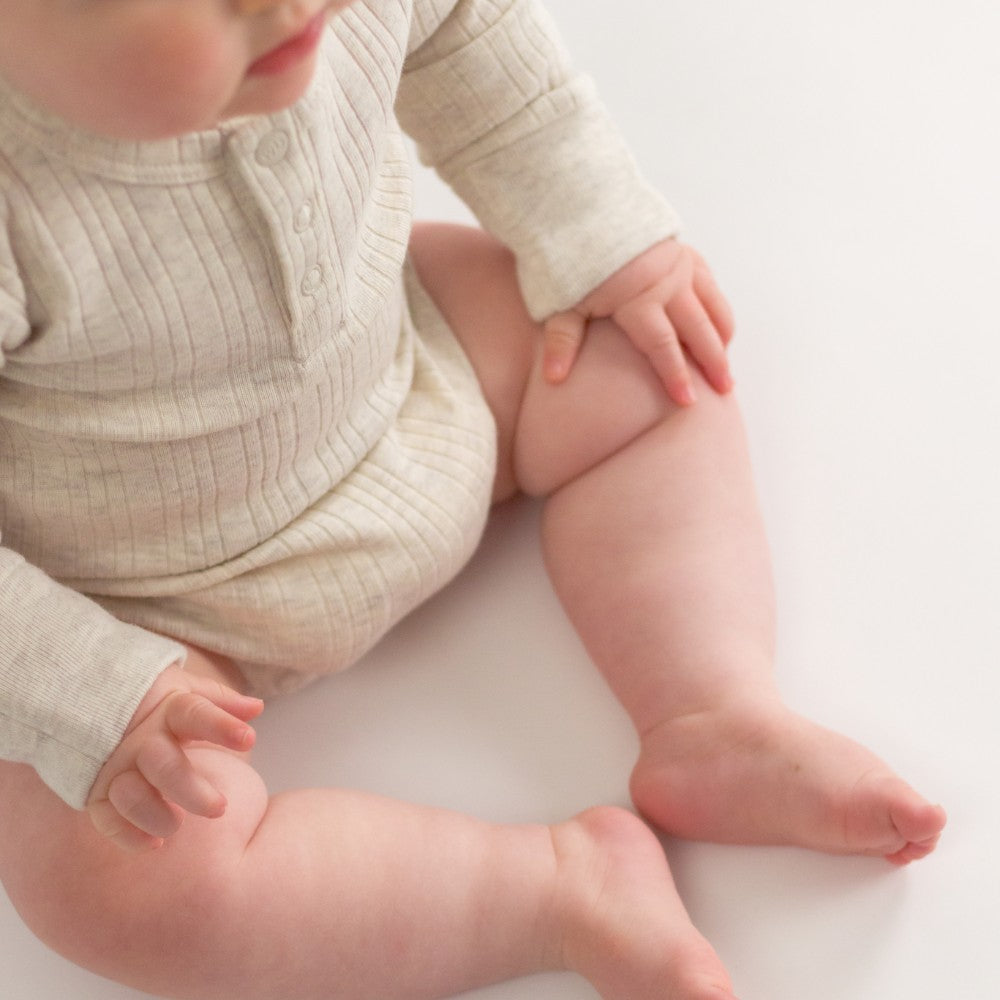 Baby in a beige woolbabe bodysuit sitting on a white surface