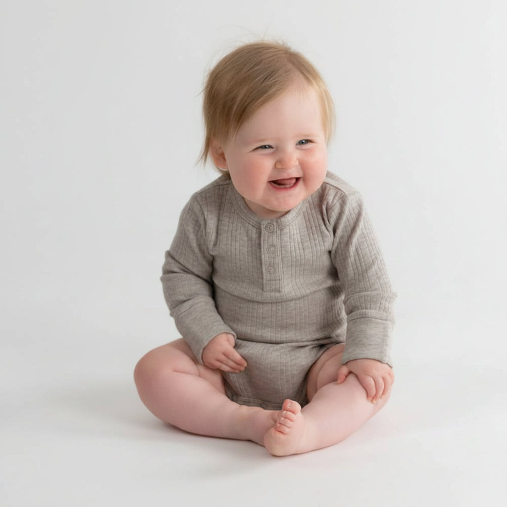 Baby sitting on a white background wearing a beige onesie.