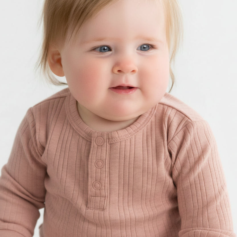 Baby wearing a pink long-sleeve rib bodysuit against a white background
