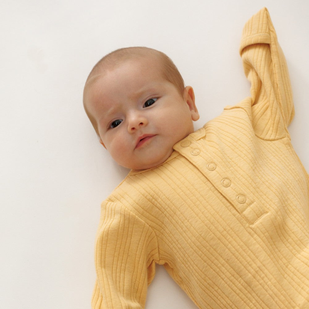 Baby wearing a yellow ribbed onesie on a white background