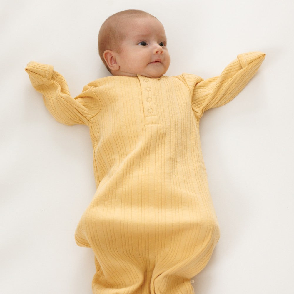Baby wearing a yellow ribbed babygown with foldover mittens e on a white background