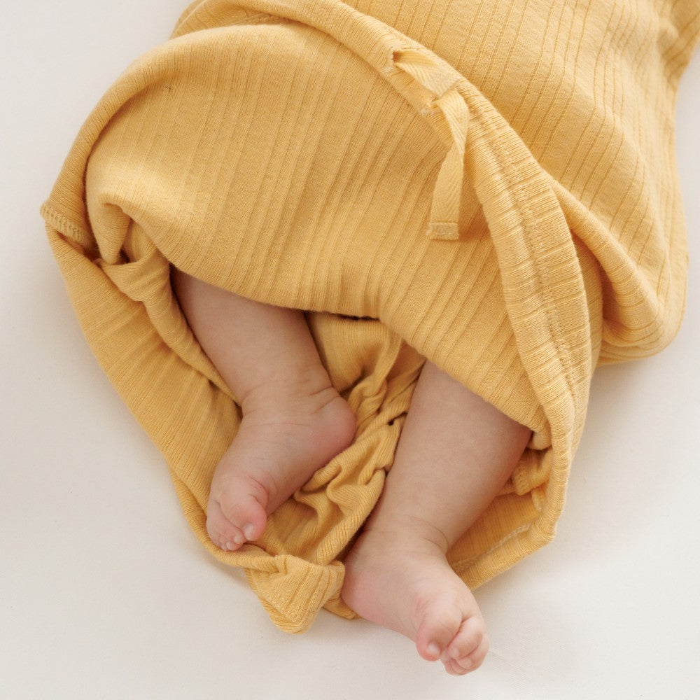 Baby feet peeking out from under a yellow baby gown n a white background