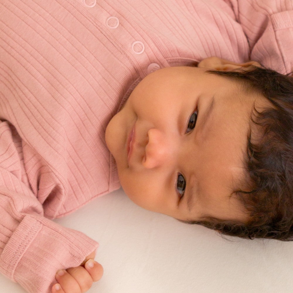 Baby wearing a pink merino baby gown lying on a white surface
