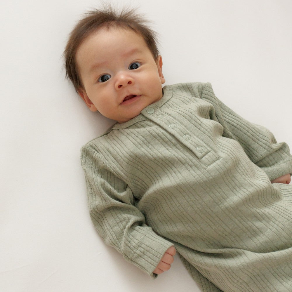 Baby wearing a green ribbed baby gown on a white background