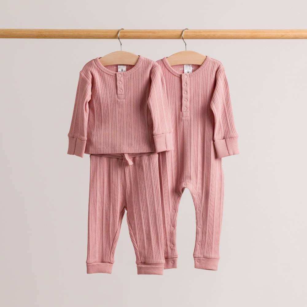 Pink woolbabe merino rib baby outfit set on hangers against a light gray background