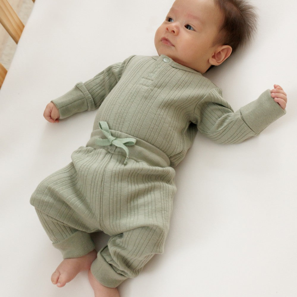 Baby wearing a green woolbabe outfit lying on a white surface
