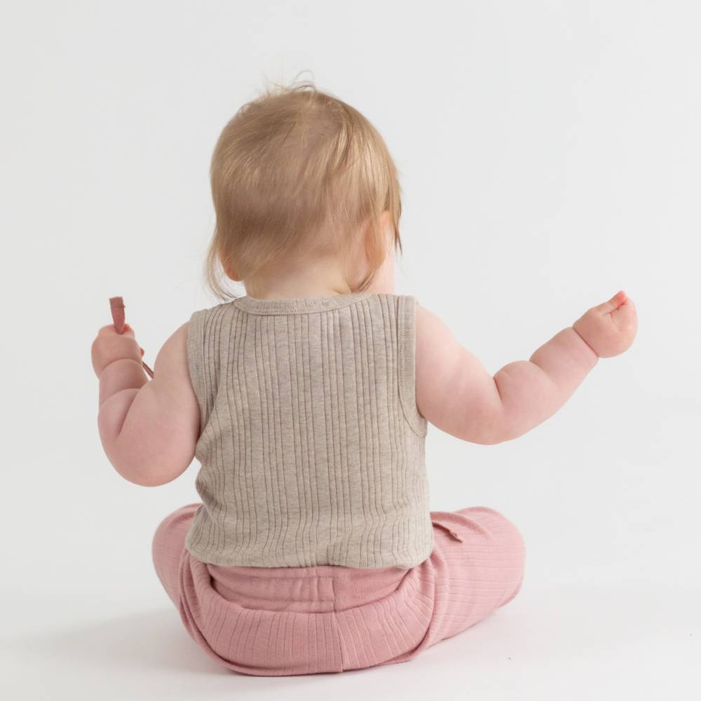 Baby wearing a beige ribbed singletsuit and pink pants on a white background