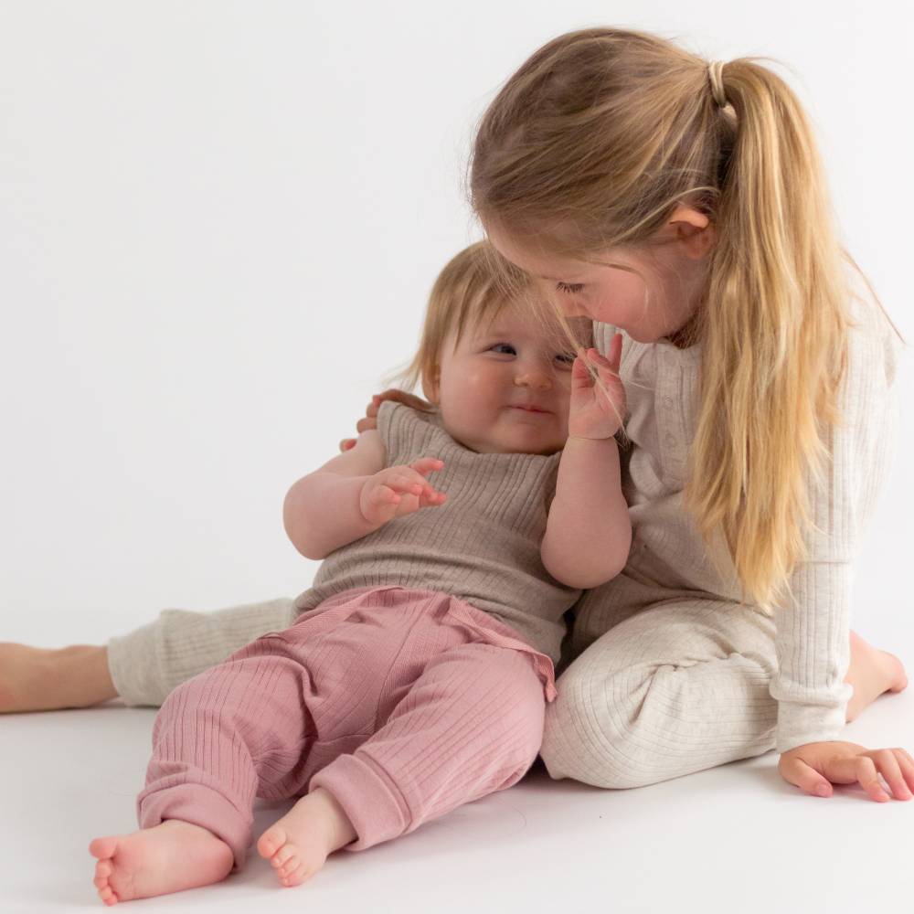 Two young children sitting on a white surface, one holding the other's face.