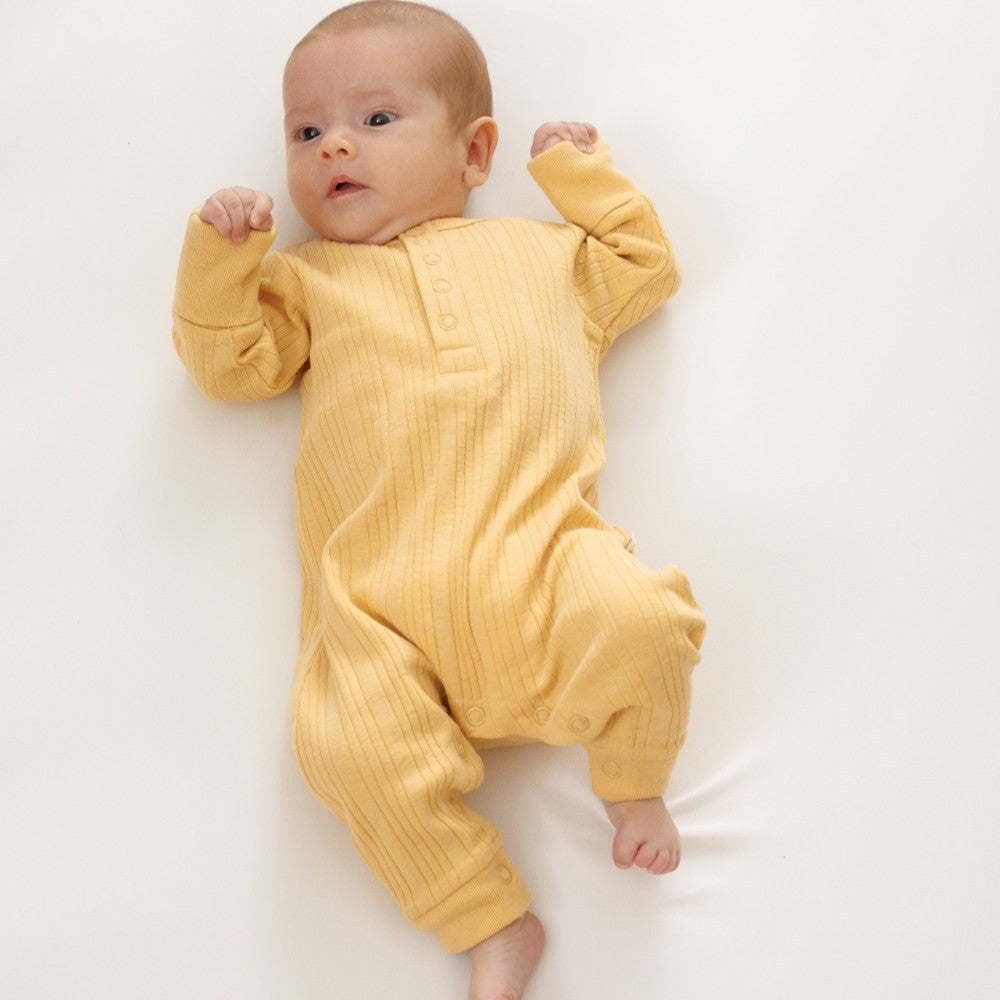 Baby wearing a yellow onesie with crotch snaps on a white background