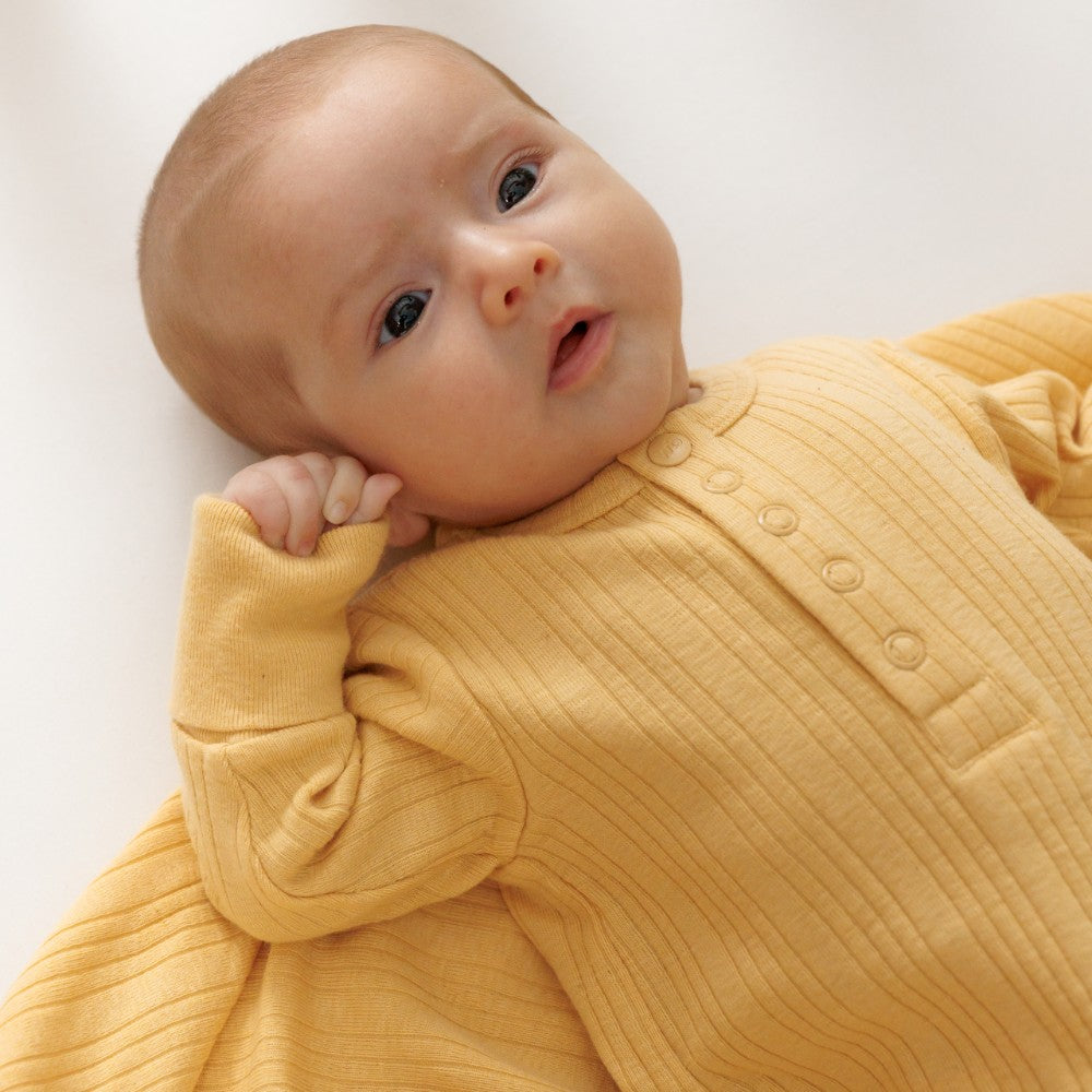Baby wearing a yellow ribbed outfit on a white background