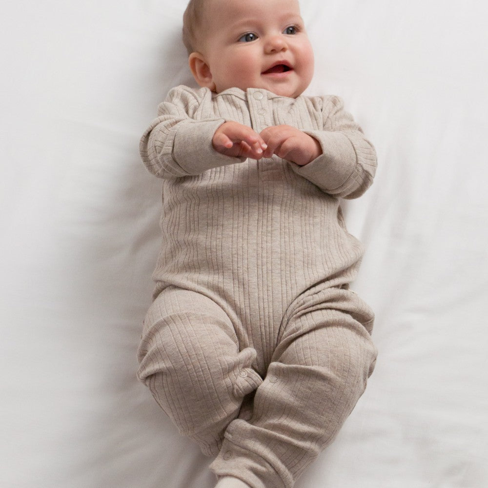 Baby wearing a beige merino onesie on a white background