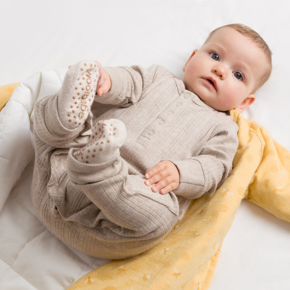 Baby in a beige outfit lying on a yellow blanket