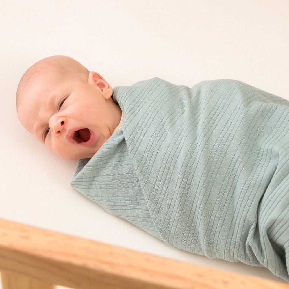 Newborn baby swaddled in a light blue blanket on a white surface.