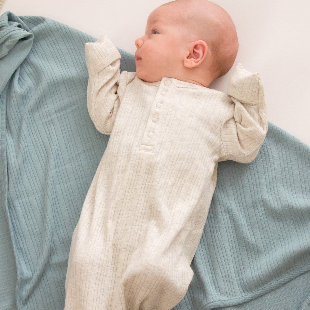 Baby in a beige outfit lying on a light blue textured blanket