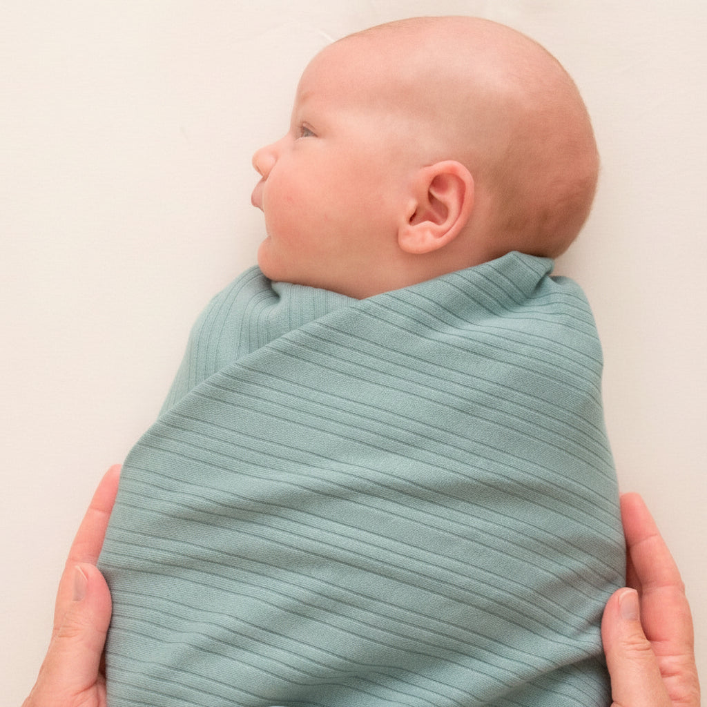 Baby wrapped in a light teal woolbabe swaddle blanket with a neutral background