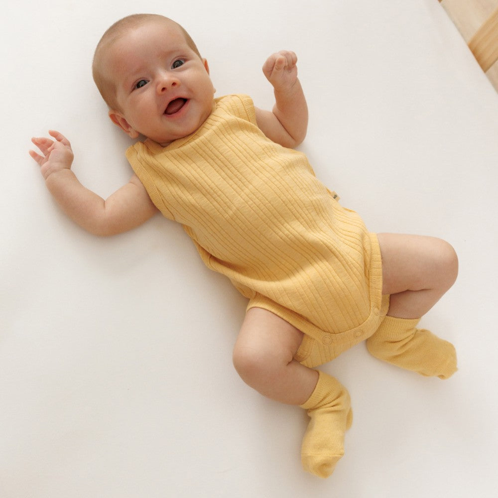 Baby wearing a yellow woolbabe buttercup singletsuit lying on a white surface