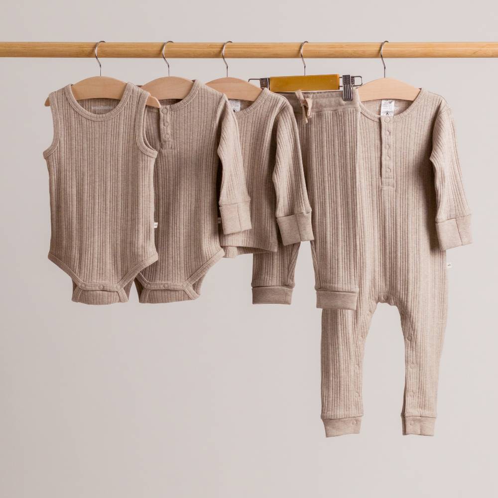Set of Dune marl woolbabe baby clothes including rompers and pants hanging on a rack against a plain background.