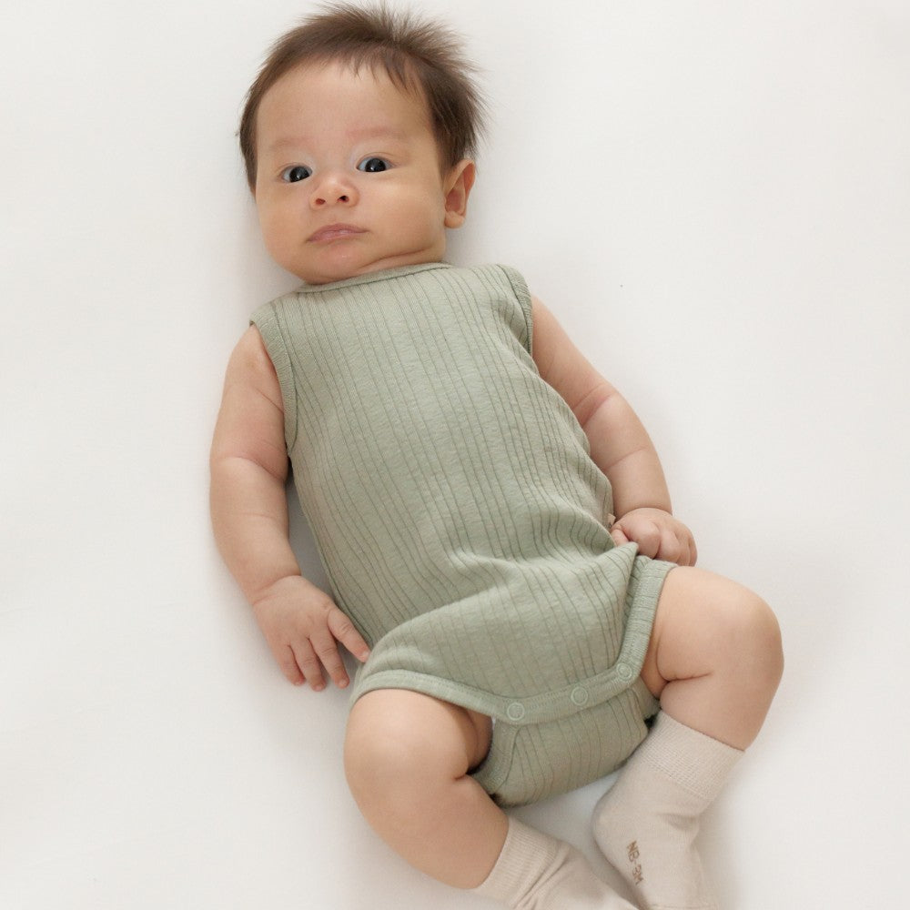 Baby wearing a green sleeveless bodysuit on a white background