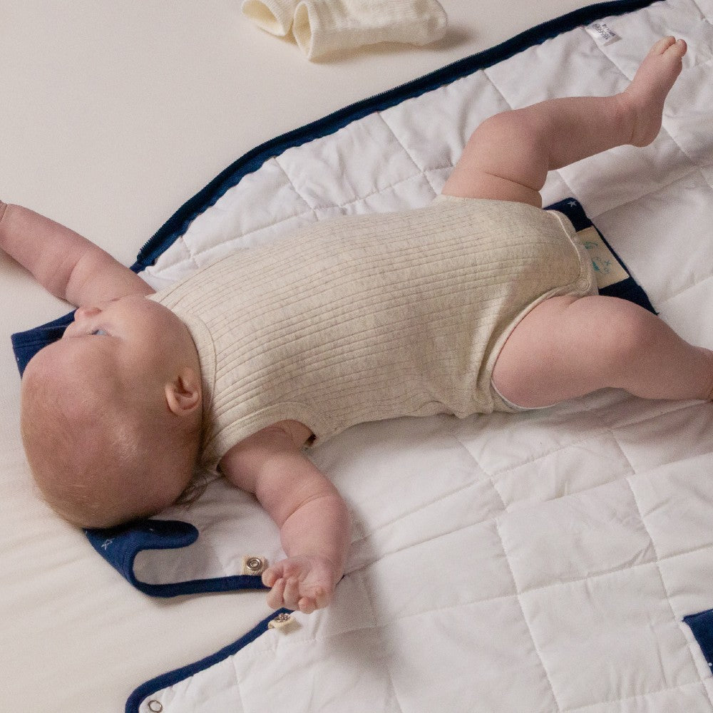 Baby lying on a  duvet mini woolbabe sleeping bag wearing a beige singletsuit