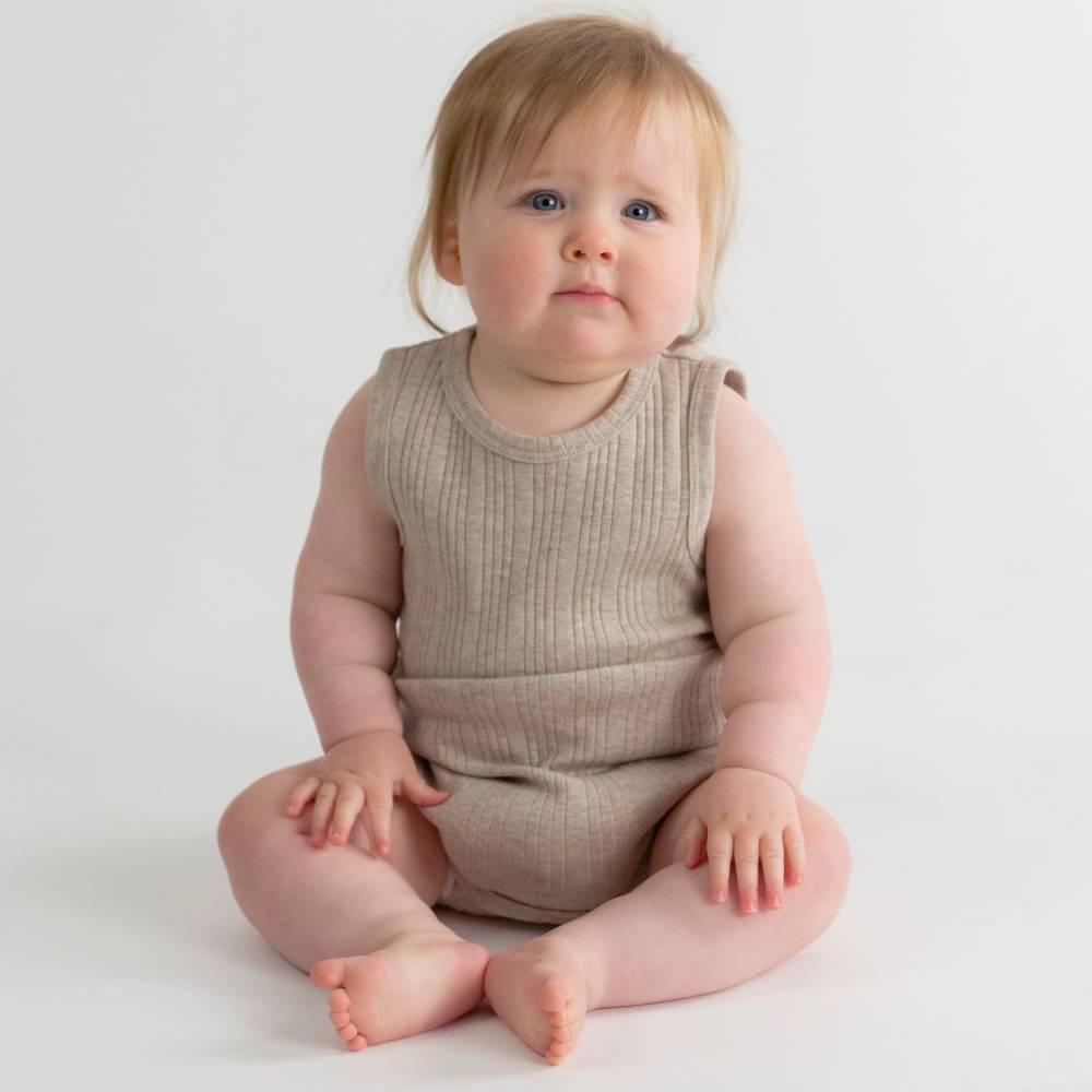Baby wearing a beige woolbabe sleeveless bodysuit sitting on a white background