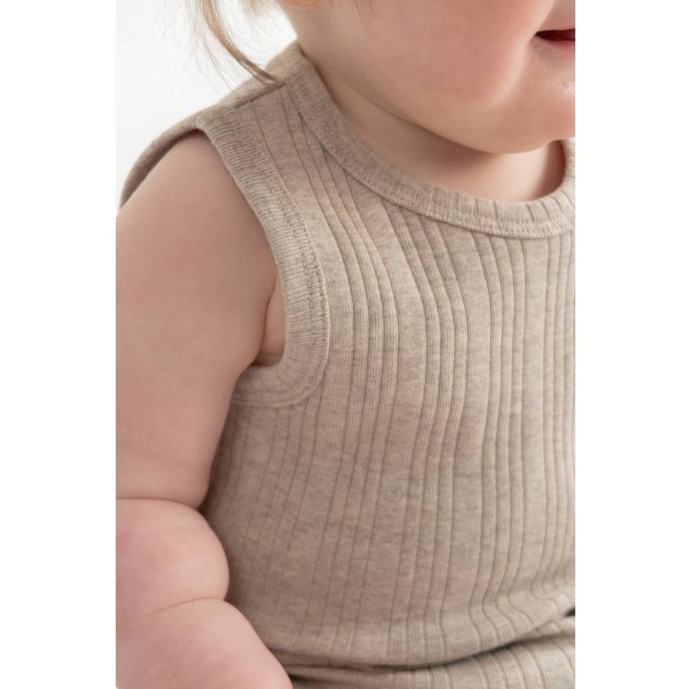 Close-up of a child wearing a beige ribbed dress on a white background