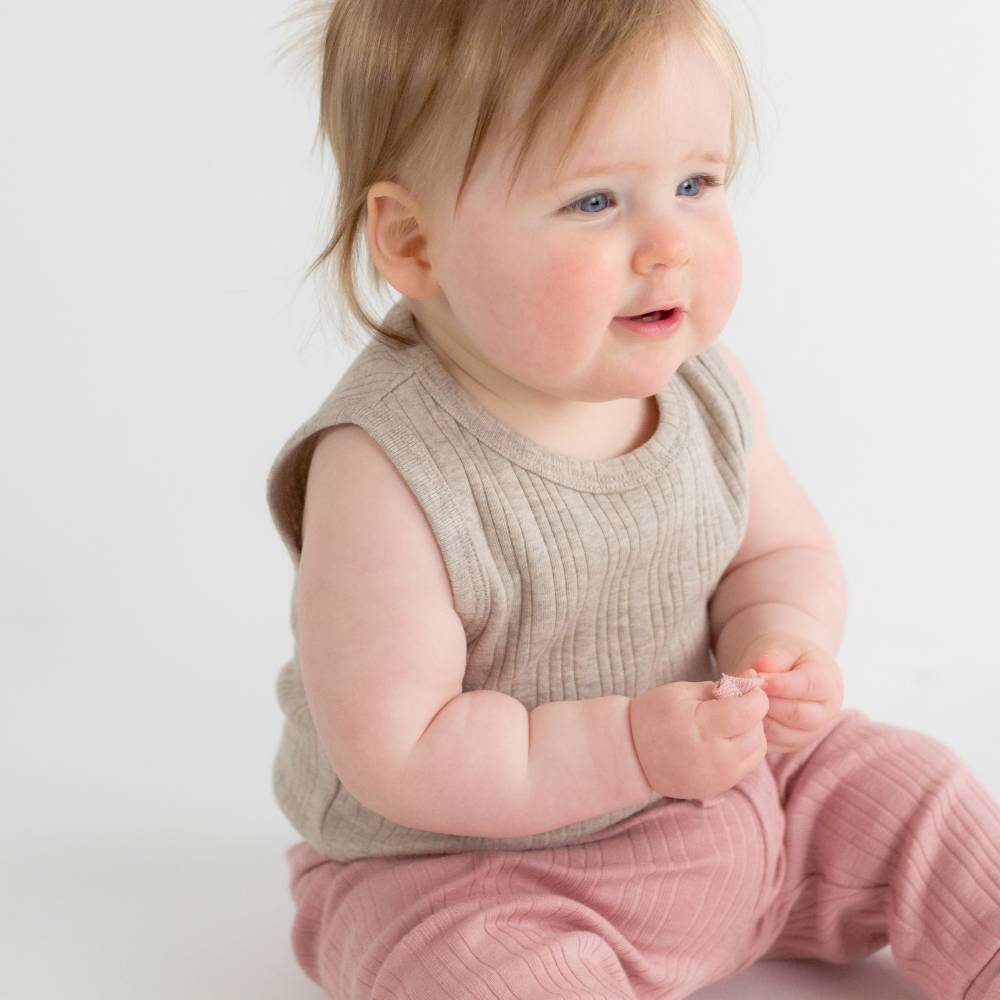 Baby wearing a beige sleeveless top and pink pants on a white background