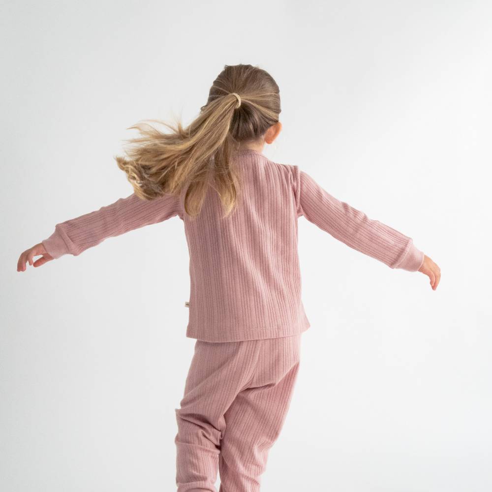 Child wearing pink ribbed pajamas against a white background