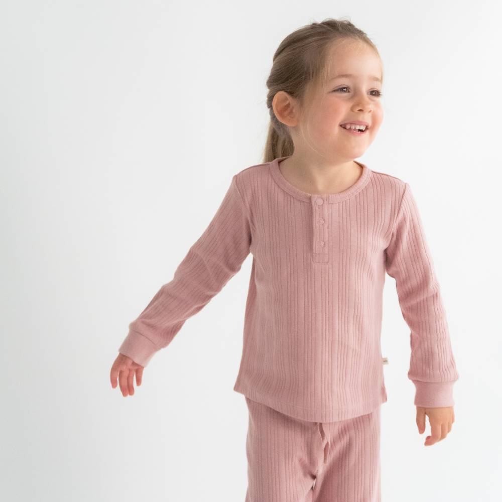 Child wearing pink ribbed pajamas on a white background