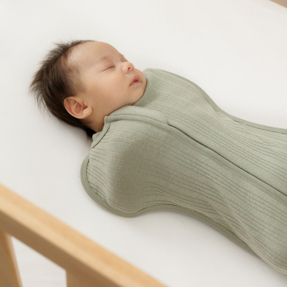 Newborn baby swaddled in a green woolbabe merino zip swaddle on a white background