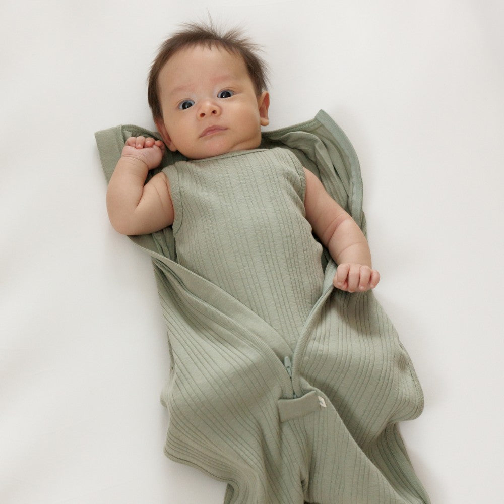Newborn baby swaddled in a green woolbabe merino zip swaddle on a white background