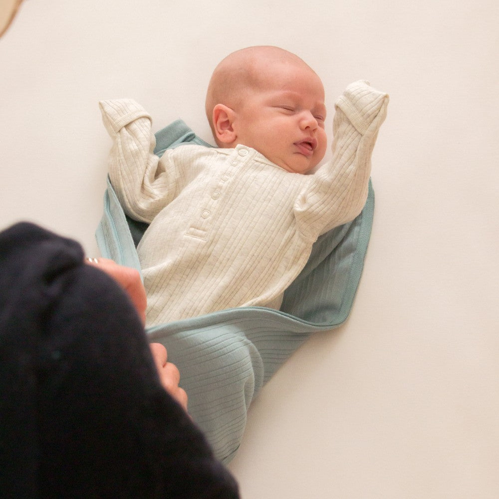 Newborn baby wrapped in a white blanket lying on a light surface