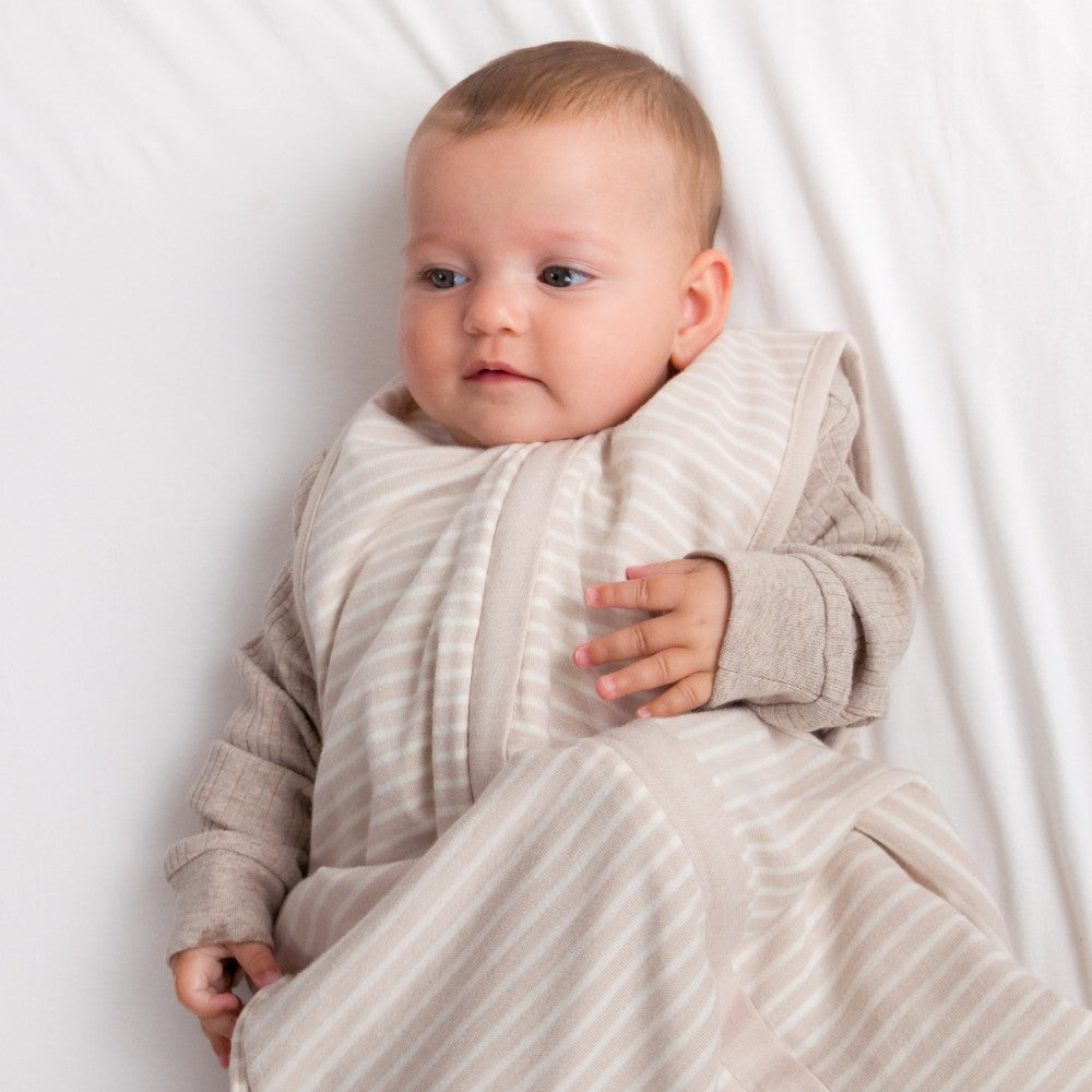 Baby wrapped in a beige striped sleep sack on a white background