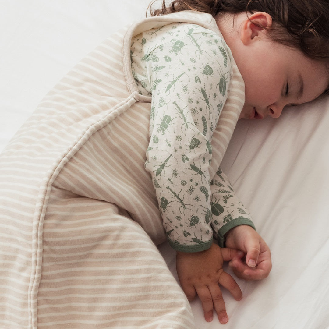 Child sleeping in a cozy beige sleeping bag with green patterned sleeves.