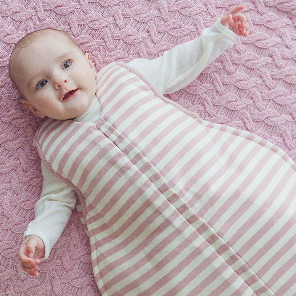 Baby wrapped in a pink and white striped sleeping bag on a pink textured blanket