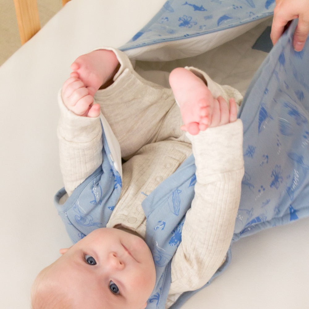 Baby lying on a blue and white patterned blanket with beige pants.