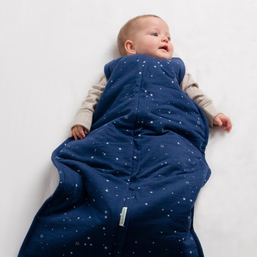 Baby lying on a white surface wearing a blue star-patterned sleeping bag