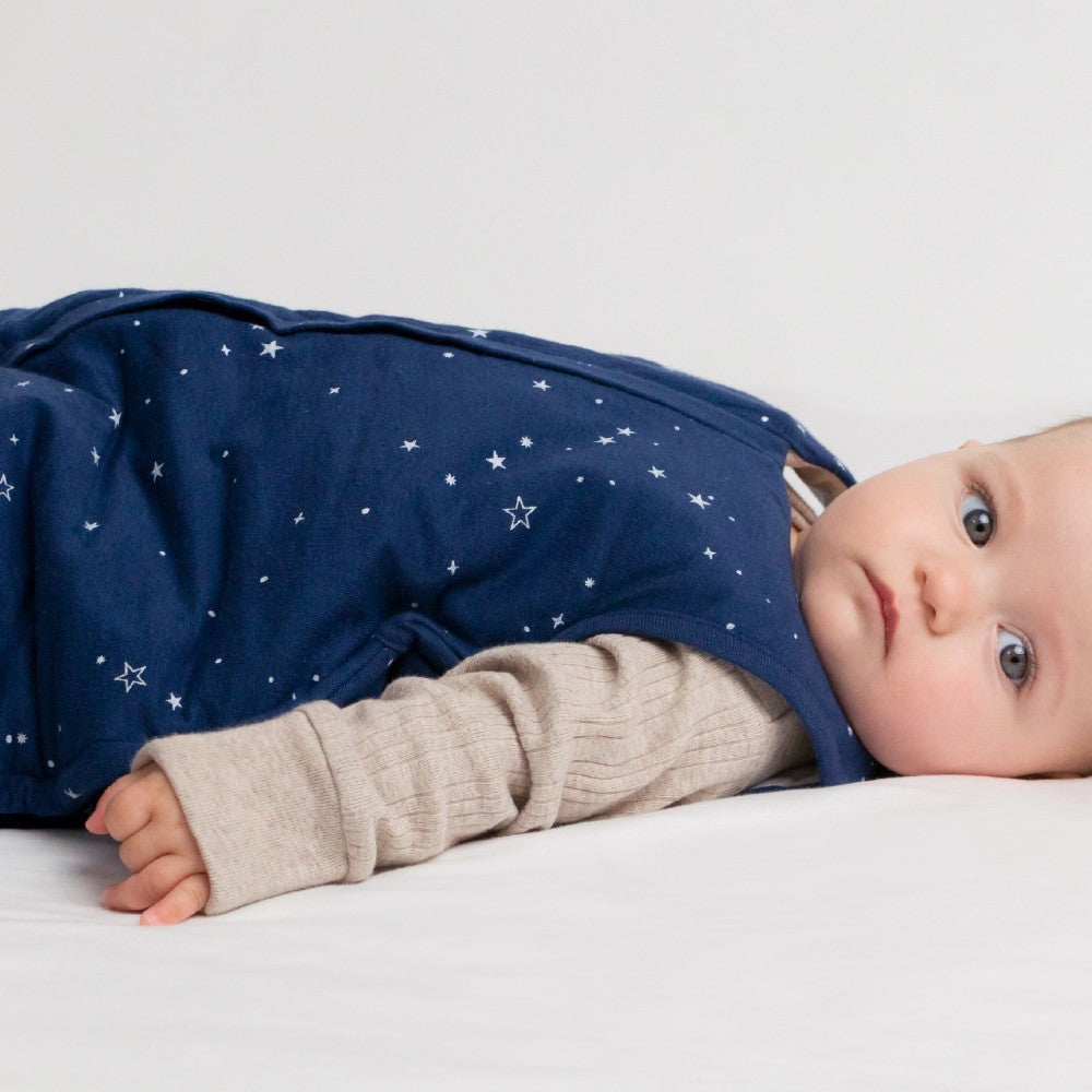 Baby lying on a white surface wearing a navy blue outfit with star patterns