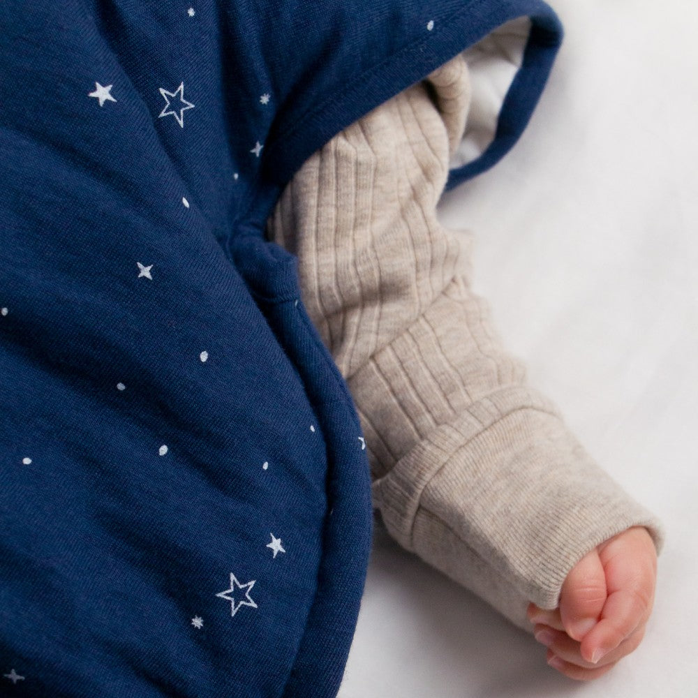 Close-up of a baby's hand and foot wearing a blue garment with star patterns and beige pants on a white background.