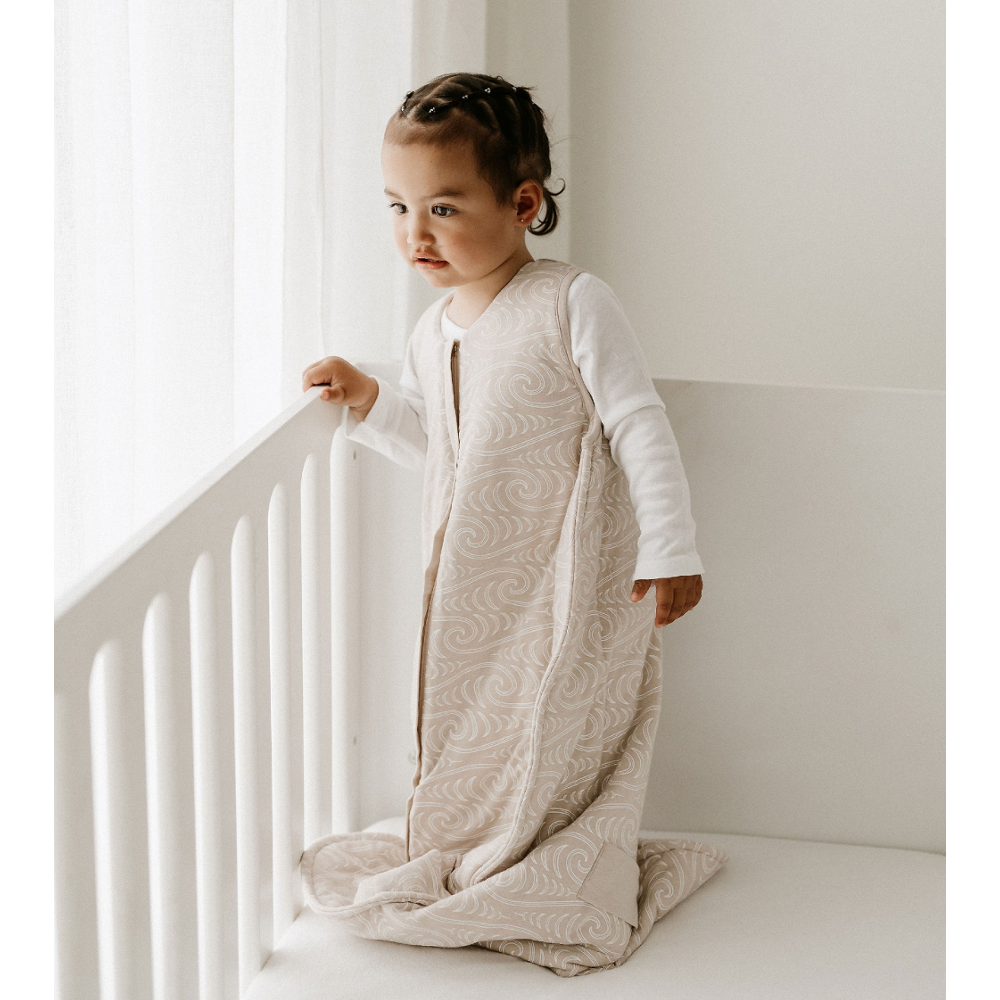 Child wearing a beige sleeping bag in a minimalistic room
