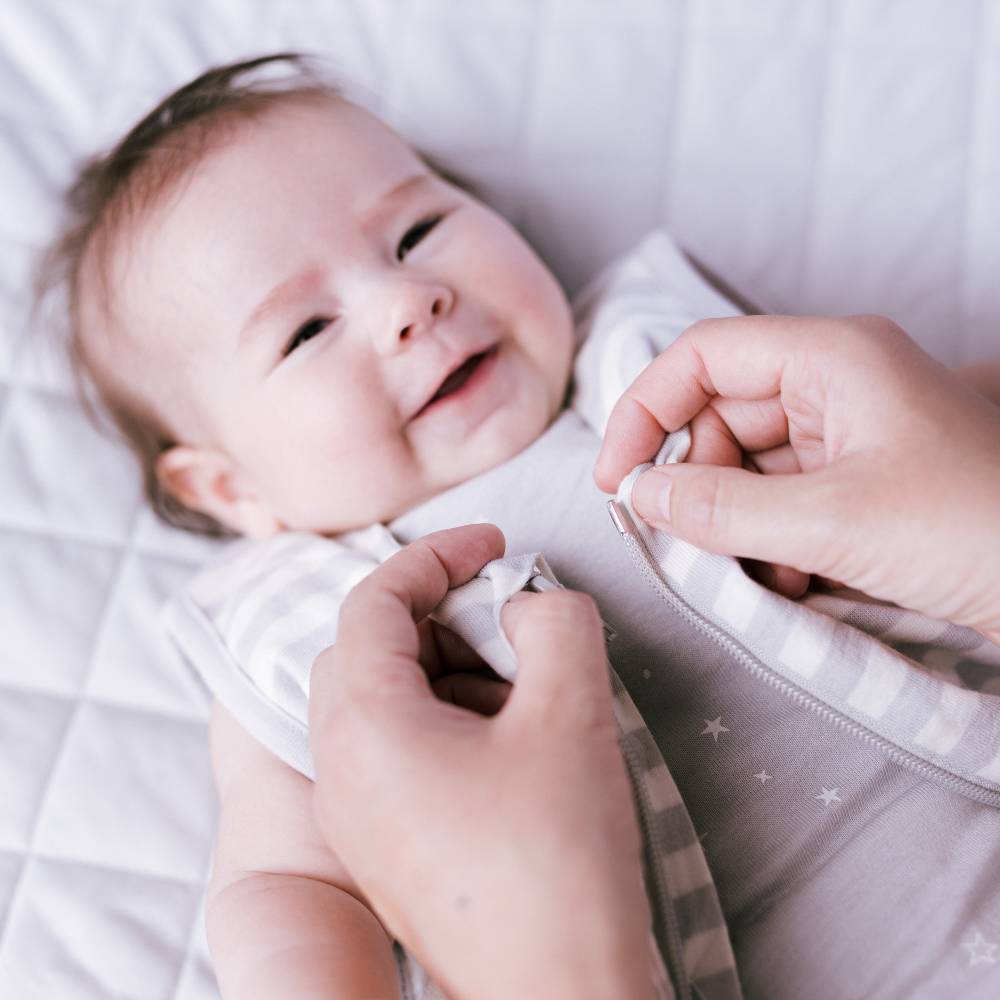 Baby being zipped into a woolbabe by a person's hands on a white blanket