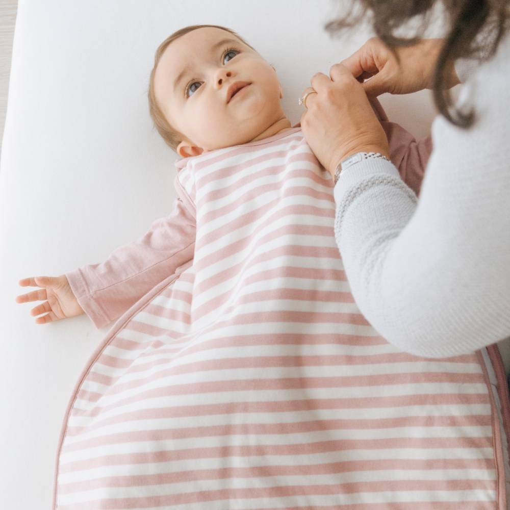Baby in a pink and white striped swaddle being held by an adult on a light background