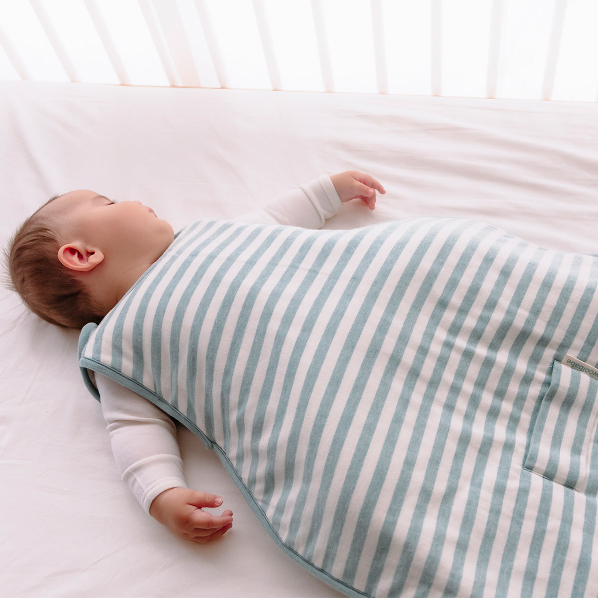 Baby wrapped in a blue and white striped swaddle on a white bed.
