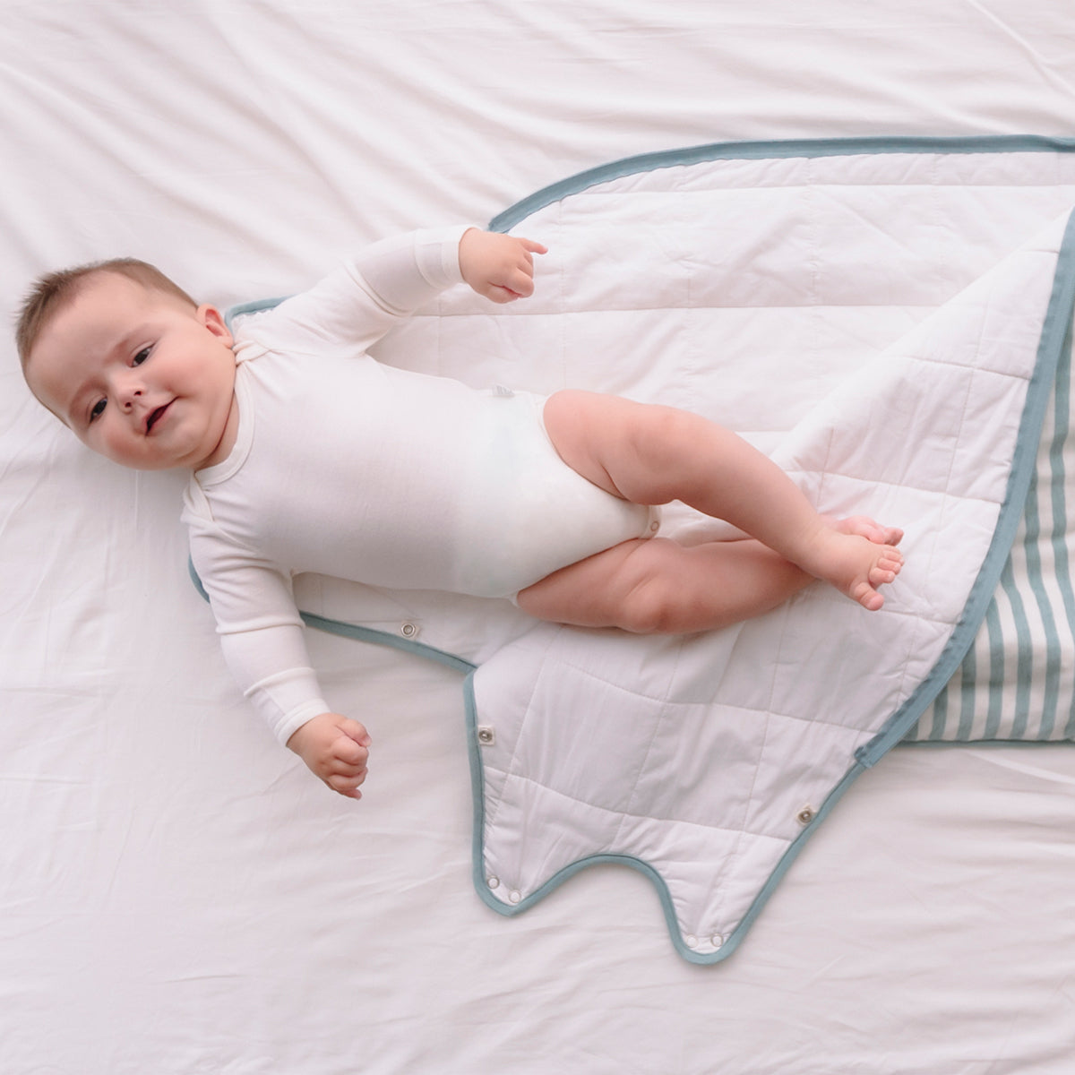 Baby lying on a white quilt with blue trim on a white background